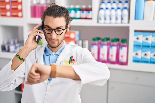 Young Hispanic Man Pharmacist Talking Smartphone Looking Watch Pharmacy — Stock Photo, Image