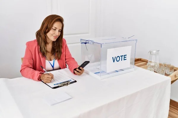 Young Latin Woman Writing Checklist Using Smartphone Working Electoral College — Stockfoto