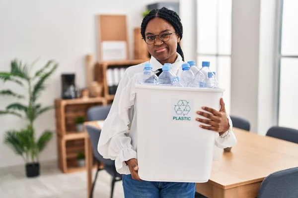 アフリカ系アメリカ人の女性は 懐疑的で緊張したリサイクルのためにペットボトルを持ってオフィスで働いており 問題のために動揺しています 否定的な人 — ストック写真