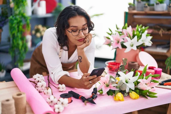 年轻美丽的惊慌失措的女花匠在花店用智能手机靠在桌子上 — 图库照片