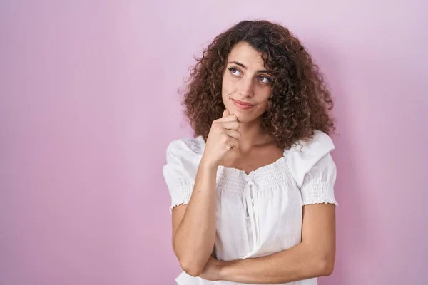 Hispanic Woman Curly Hair Standing Pink Background Hand Chin Thinking — Zdjęcie stockowe