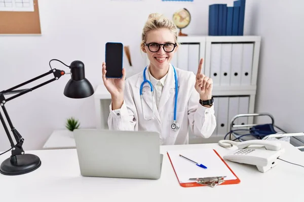 Joven Doctora Sosteniendo Teléfono Inteligente Mostrando Pantalla Blanco Sonriendo Con — Foto de Stock