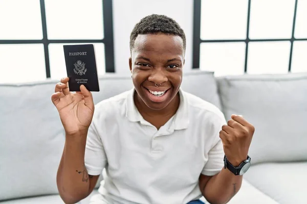 Young african man holding united states passport screaming proud, celebrating victory and success very excited with raised arms