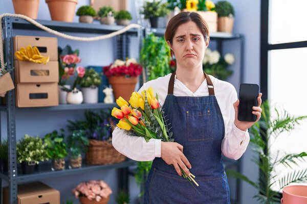Brunette woman working at florist shop holding smartphone depressed and worry for distress, crying angry and afraid. sad expression. 