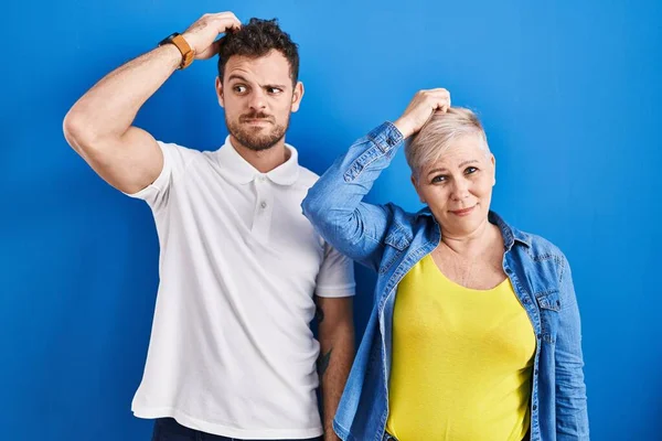 青い背景の上に立つ若いブラジル人の母親と息子は混乱し 疑問に思っています 疑いもなく頭に手を置いて考える 包括的な概念は — ストック写真