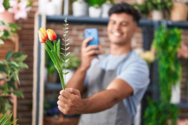 Young hispanic man florist make photo to flower by smartphone at flower shop