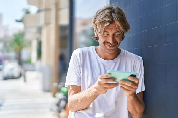 Young blond man smiling confident watching video on smartphone at street