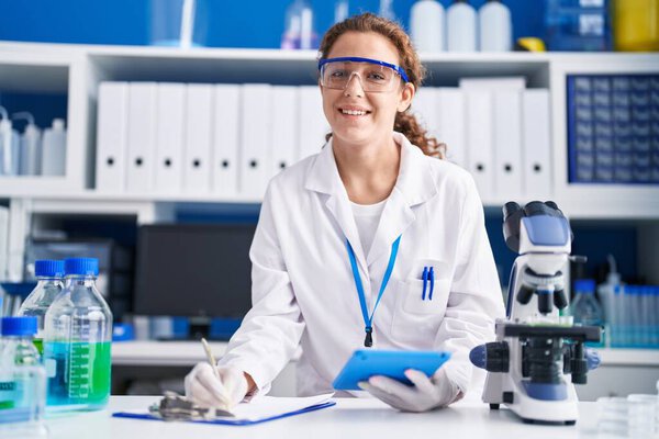 Young beautiful hispanic woman scientist using touchpad writing on document at laboratory