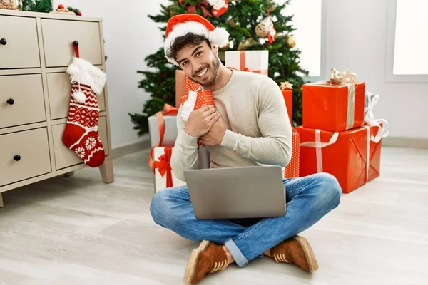 Jovem Hispânico Homem Sorrindo Feliz Segurando Presente Natal Usando Laptop — Fotografia de Stock