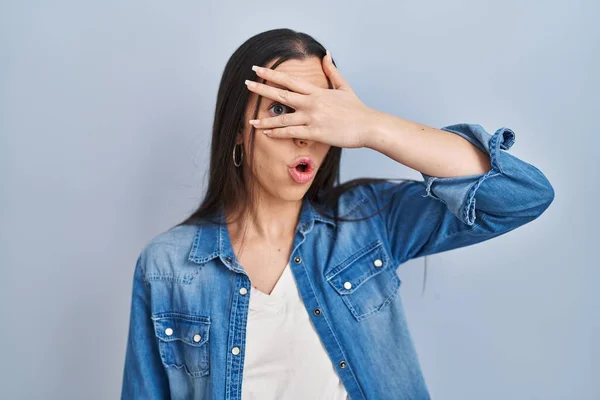 Mujer Hispana Pie Sobre Fondo Azul Asomándose Shock Cubriendo Cara —  Fotos de Stock