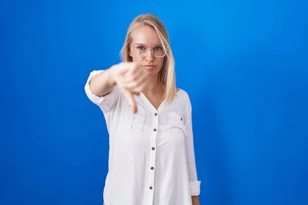 年轻的高加索女人站在蓝色的背景上 看起来很不高兴 很生气 用拇指低下的姿势表示拒绝和消极 不好的表达方式 — 图库照片
