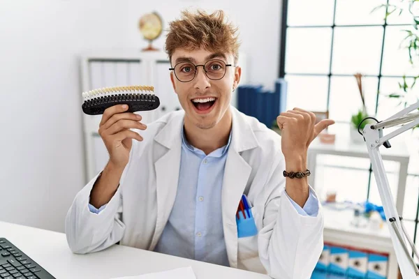 Young Caucasian Dentist Man Comparing Teeth Whitening Clinic Pointing Thumb — Stok fotoğraf