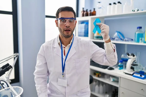 青いリボンを持っている科学研究所で働いてひげを生やして若いヒスパニック系の男は怖がって 驚きのために口を開けて驚いて 不信の顔 — ストック写真