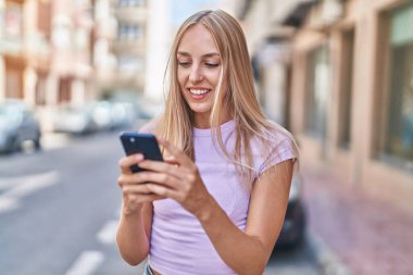 Sokakta akıllı telefon kullanan, kendine güvenen genç sarışın kadın.