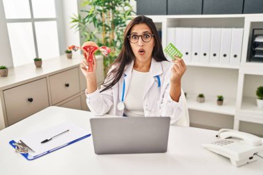 Genç İspanyol doktor kadın anatomik kadın organı ve doğum kontrol hapları tutuyor. Şaşırmış ve şaşırmış bir ifade, korku ve heyecanlı bir yüz ifadesi var.. 