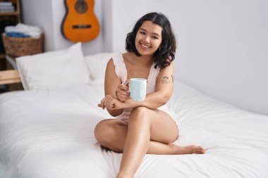 Genç bir kadın yatak odasında bir fincan kahve içiyor.