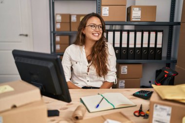 Küçük işletme şirketinde çalışan genç İspanyol kadın yüzünde gülümseme ve doğal ifadeyle yan yana bakıyor. Kendinden emin gülen. 