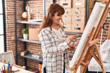 Sanat stüdyosunda kendine güvenen orta yaşlı kadın sanatçı gülümsüyor.