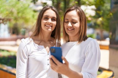 Two women mother and daughter using smartphone at park