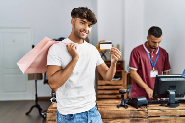 Genç İspanyol müşteri alışveriş çantası ve kredi kartını giyim mağazasında tutuyor..