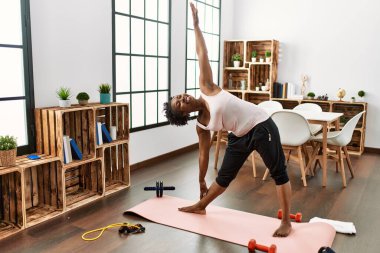 Afro-Amerikalı kadın gülümseyerek evde yoga eğitimi alıyor.