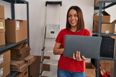 Young beautiful hispanic woman ecommerce business worker using laptop standing at office