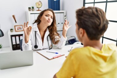 Young doctor woman showing electronic cigarette and normal cigarrete to patient looking at the camera blowing a kiss being lovely and sexy. love expression. 
