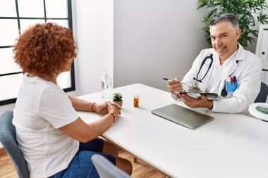 Doktor üniforması giyen orta yaşlı bir adam ve kadın klinikte tıbbi danışmanlık yapıyorlar.