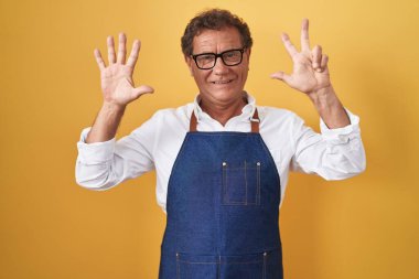 Middle age hispanic man wearing professional cook apron showing and pointing up with fingers number eight while smiling confident and happy. 