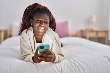 Afrika kökenli Amerikalı bir kadın yatakta akıllı telefon kullanıyor.