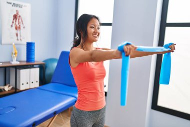 Young chinese woman patient having rehab session using elastic band at rehab clinic