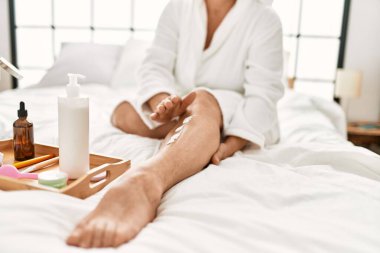 Yatak odasındaki yatakta oturan, cilt kremi kullanan bir kadın..