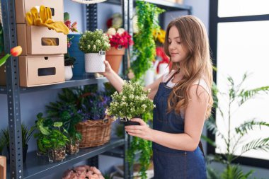 Young woman florist smiling confident holding plant at florist shop