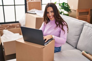Young hispanic woman smiling confident using laptop at new house