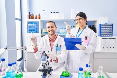 Bilimadamı laboratuvarında çalışan iki genç mutlu bir şekilde el ve parmak kenarı işaret ediyor. 