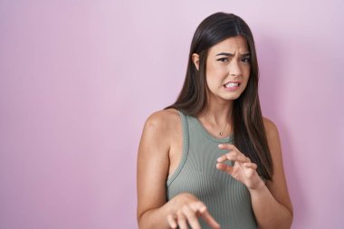 İspanyol kadın pembe arka planda duran tiksindirici ifade, tiksindirici tepki yüzünden tiksinti ve korku dolu yüz ifadesi. Eller havada. 