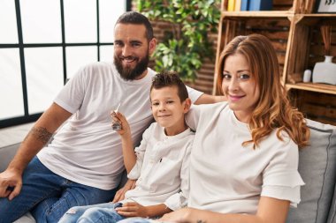 Family holding key of new house hugging each other sitting on sofa at home