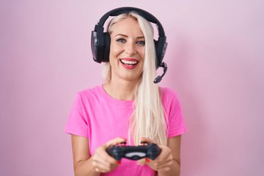 Caucasian woman playing video game holding controller smiling and laughing hard out loud because funny crazy joke. 