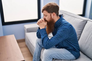 Young redhead man stressed sitting on sofa at home