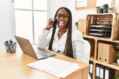 Ofiste örgü ören zenci kadın telefonda konuşuyor ve komik bir ifadeyle dilini dışarı çıkarıyor. duygu kavramı. 