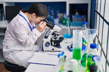 Young woman with down syndrome scientist using microscope at laboratory