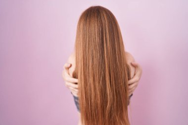 Kızıl saçlı kadın pembe arka plan üzerine iç çamaşırı giyip kendine sarılıyor mutlu ve pozitif bir şekilde. Sevgi ve özgüven. 