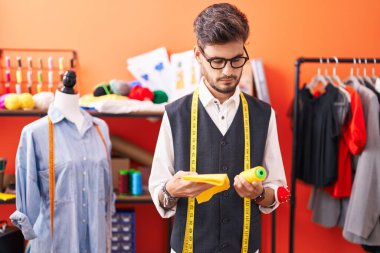 Genç İspanyol terzi atölyede kumaş ve iplik tutuyor.