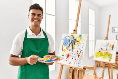 Genç İspanyol adam resim stüdyosunda kendine güvenen gülümsüyor.