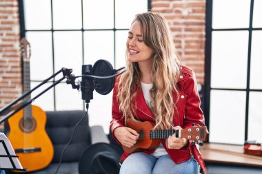 Müzik stüdyosunda ukulele çalan genç bir müzisyen kadın.