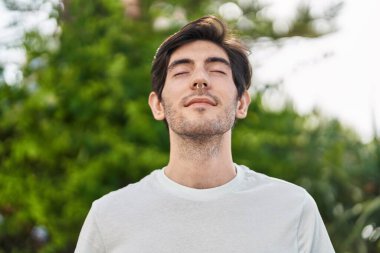 Young hispanic man breathing with closed eyes at park