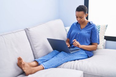 African american woman using laptop sitting on sofa at home