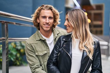 Kadın ve erkek gülümsüyor. Kendilerine güveniyorlar. Sokakta sarılıyorlar.