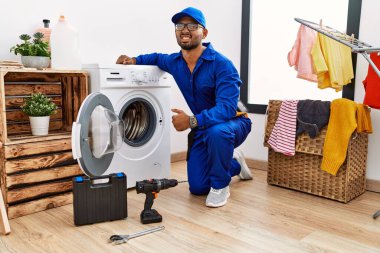 Young indian technician working on washing machine angry and mad screaming frustrated and furious, shouting with anger. rage and aggressive concept. 