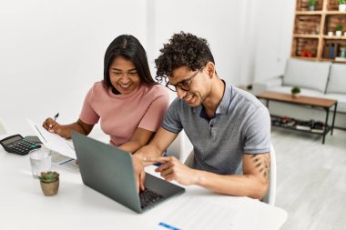 Genç Latin çift evde masada dizüstü bilgisayar kullanarak çalışıyor..